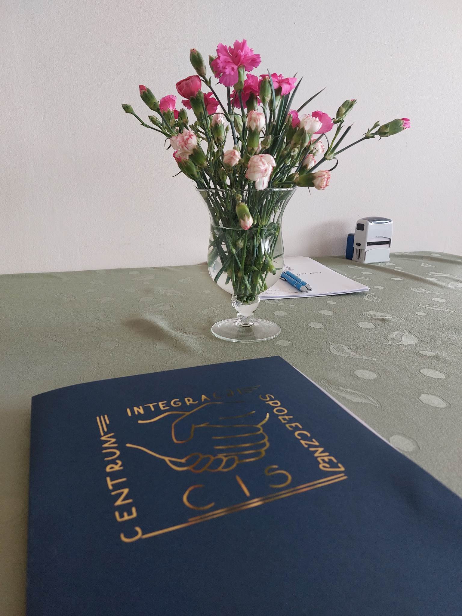 na tle kwiatów teczka granatowa z logo Centrum Integracji Społecznej w Chełmie na tle kwiatów teczka granatowa z logo Centrum Integracji Społecznej w Chełmie